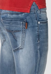 Hellblaue Jeans mit verblasstem Finish, versehen mit gesteppten Gesäßtaschen und einem kleinen braunen Etikett am Bund. Saumkante.