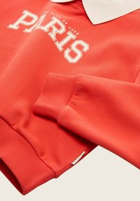 Koraal sweatshirt met een witte kraag, met "PARIS" in vetgedrukte witte letters en geribbelde mouwmanchetten. Zacht katoenmix materiaal.