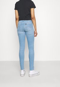 Jeans ajustados de color azul claro, hechos de denim, con una cintura de altura media y bolsillos traseros tradicionales. Combinados con zapatillas de lona blancas.