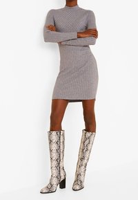 Robe en tricot côtelé gris avec un col montant, associée à des bottes au genou à imprimé serpent avec un talon épais.