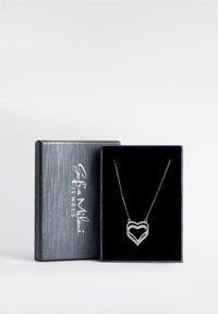 Sølv hjertevedhængs halskæde med sammenkoblede hjerter, prydet med små klare ædelsten, vist i en boks med sort fløjl inde.