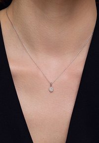 Srebrny naszyjnik z delikatnym łańcuszkiem i okrągłym zawieszką z grupą małych, błyszczących kamieni, spoczywający na obojczyku.