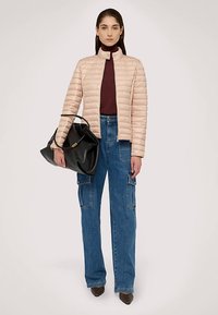 Světle růžová prošívaná bunda, bordó rolák a široké modré cargo džíny. Černá kabelka s strukturovaným designem a zlatými kovovými doplňky.