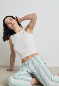 Biely rebrovaný crop top v kombinácii s svetlomodrými a bielymi pásikovanými voľnočasovými nohavicami, ktoré majú elastický pás a stužkový detail. Mäkkučký materiál.