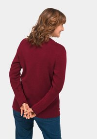 Bordeauxfarbener Langarmpullover mit Rundhalsausschnitt und seitlichen Schlitzen, kombiniert mit dunkelblauen Jeans, von hinten gezeigt.