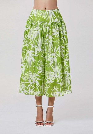 Jupe midi taille haute verte avec motif de feuilles tropicales blanches, portée avec des talons ouverts à bride cheville blancs, vue de la taille aux pieds.