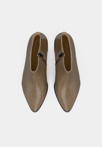 Spitz zulaufende, knöchelhohe Schuhe aus glattem taupefarbenem Leder mit einem seitlichen Reißverschluss und einer schwarzen Gummisohle. Minimalistisches Design mit abgerundeten Kanten.