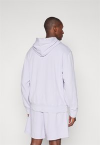 Felpa con cappuccio di un delicato colore viola, dal fit rilassato, realizzata in materiale morbido, presenta orli e polsini a coste, indossata con pantaloni corti coordinati.