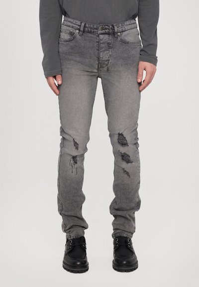 Jean en denim gris avec une finition délavée, comportant des zones usées et un design classique à cinq poches. Fabriqué en coton avec une texture subtile.