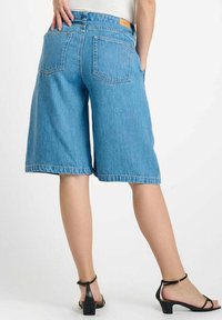 Denim bermuda-shorts in lichtblauw, met een hoge taille, losse pasvorm, achterzakken en een rauwe zoom. Gecombineerd met zwarte enkellaarsjes met een enkelbandje.