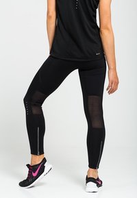 Black athletic leggings with mesh panels, slim fit design, reflective accents, and paired with black and pink athletic shoes.