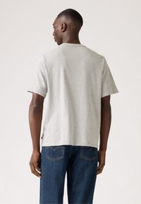 Grijze T-shirt met korte mouwen, rechte snit en ronde hals, gemaakt van een zachte stof. Draagt met blauwe denim jeans, met minimale details.