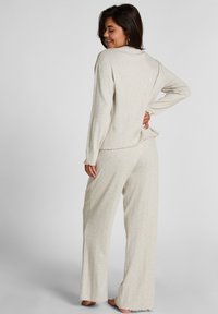 Lichtbeige lounge-outfit bestaande uit een langelijf top met een ronde zoom en bijpassende wijde broek met rafelranden. Zachte textuur.