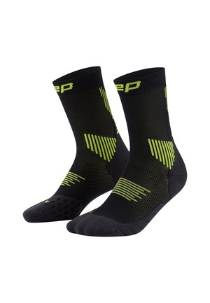 Schwarze Sportsocken mit grünen geometrischen Mustern und texturiertem Grip an den Sohlen. Entwickelt für Leistung mit einer engen Passform.