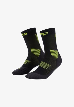 Black athletic socks with green geometric patterns and textured grip on the soles. Designed for performance with a snug fit.