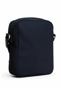 Bolso cruzado cuadrado en navy, hecho de una tela suave, que cuenta con una sola correa ajustable y detalles de costura sutiles. Sin logos visibles.
