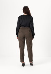 Haut noir à manches longues avec un col rond, associé à un pantalon marron à motifs. Le pantalon a une taille élastique et des jambes fuselées.