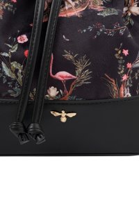 Sac à cordon avec un motif floral et des flamants roses sur un fond sombre, base en cuir noir et accent en abeille dorée.