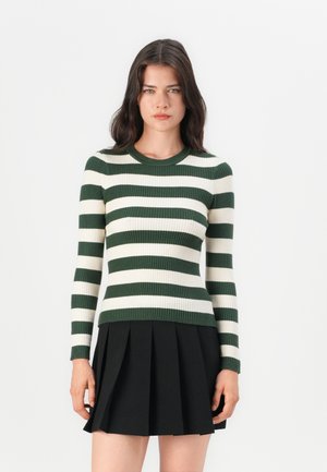 Pull rayé vert et blanc à côtes avec un col rond et des manches longues, porté avec une jupe plissée noire.