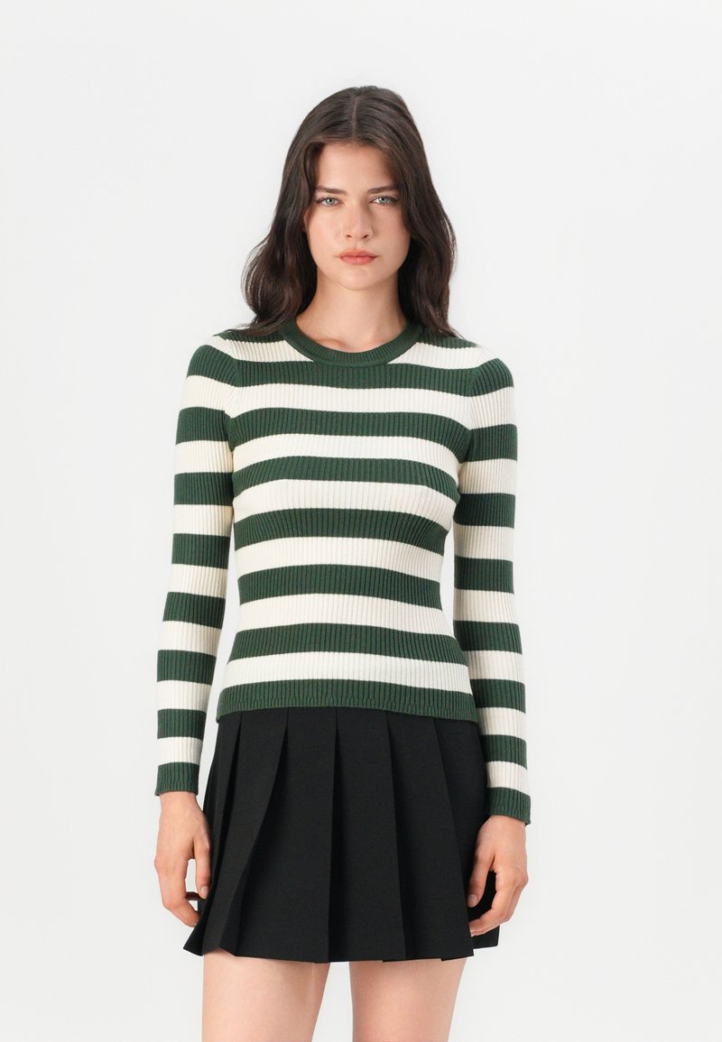 Groen en wit gestreepte ribbeltop met een ronde hals en lange mouwen, gedragen met een zwarte geplisseerde rok.