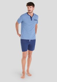 Camisa de manga corta a rayas en azul y blanco con cuello redondo y bolsillo, combinada con pantalones cortos lisos en color marino. Tejido de algodón, ajuste casual.