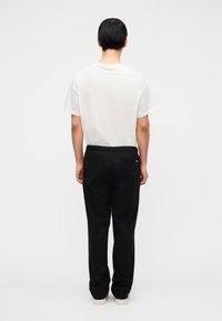 Pantalon noir à coupe décontractée, taille élastique et deux poches arrière. Associé à un t-shirt blanc uni. Fond uni.