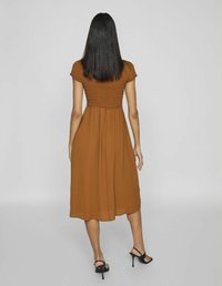 Rochie maro, de lungime medie, cu un corset plisat și mâneci scurte. Material neted și ușor; asociată cu sandale negre cu toc.