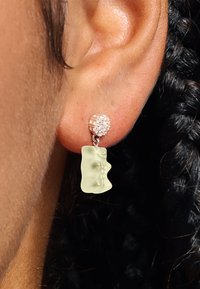 Ohr mit hängendem Ohrstecker, der einen Cluster aus kleinen klaren Steinen und einen durchscheinenden, blassgelben Gummibärchen-Anhänger zeigt.