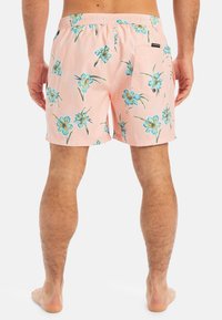 Rosa Badehose mit floralem Muster, das blaue Blumen und grüne Blätter zeigt. Elastischer Bund mit einer Rückentasche.
