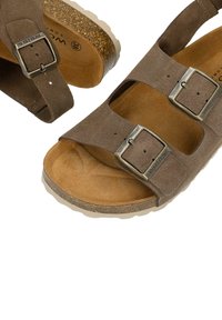 Sandales en daim marron avec double boucle métallique réglable et semelles en liège moulées sur fond blanc.