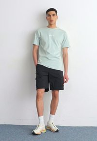 Lys blå t-skjorte med logo, svarte cargo-shortser, hvite ankelsokker og flerfargede joggesko med reflekterende detaljer.