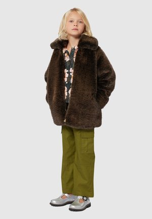 Bruine nepbontjas met een brede kraag, bloemenpatroon shirt, olijfgroene cargobroek en zilveren Mary Jane schoenen met een bloemaccent.