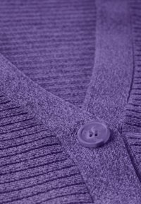 Lila kofta med en strukturerad, ribbad design och en mjuk finish, samt en platt knappstängning vid halsen.