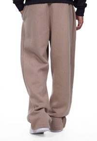 Beige sweatpants made of soft material with a relaxed fit, featuring a wide leg design and subtle side seams. White athletic shoes visible.