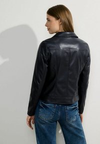 Giubbotto in pelle nera con colletto classico e design aderente. Tessuto liscio, progettato con cuciture verticali e dettagli hardware minimi.