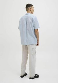 Camisa de manga corta azul claro con un pliegue en la espalda, combinada con pantalones cargo gris claro que tienen bolsillos laterales y sandalias negras.