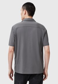 Polo gris de manga corta hecho de una tela suave, con un cuello clásico, dobladillo recto y detalles de costura mínimos.