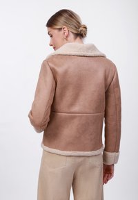 Brun faux shearling-jakke med en beige krage og mansjetter, som har en jevn tekstur og tilpasset design, sett fra baksiden.