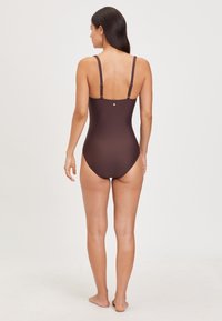 Brauner einteiliger Badeanzug mit verstellbaren Trägern, glatter Textur, hoch geschnittenen Beinen und einem kleinen metallischen Akzent hinten.