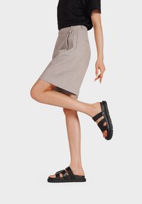 Sandali neri con due ampie cinghie e suole testurizzate abbinati a una gonna grigia chiara a lunghezza ginocchio con pieghe e tasche laterali.