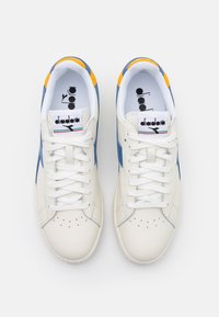 Vita lädersneakers med blå och gula accenter, vita snören och Diadora-logotyp på tungan och innersulan, visade från ovan.
