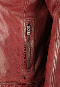 Rote Lederjacke mit Nahaufnahme einer Reißverschlusstasche, die aus strukturiertem Material besteht und detaillierte Nähte entlang der Kanten aufweist.