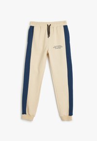 Beige sweatrokken met marineblauwe gestructureerde zijkanten, elastische tailleband met trekkoord en bedrukte tekst aan de voorkant in contrasterende kleur.