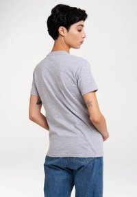 Graues T-Shirt mit kurzen Ärmeln, gefertigt aus einem weichen Stoff, mit Rundhalsausschnitt und lässiger Passform. Sichtbares Tattoo am Arm. Blaue Jeans im Bild.