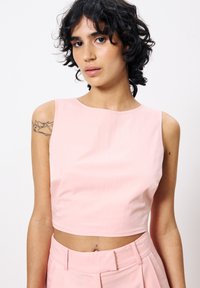 Rosa Crop-Top mit glatter Textur und ärmellosem Design. Verfügt über einen runden Ausschnitt und eine figurbetonte Form, kombiniert mit hochtaillierten Hosen.