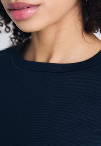 Navy ribbed knit top featuring a round neckline and subtle stitching details, showcasing a soft texture and close-fitting design.