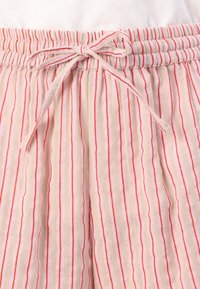 Shorts en tissu beige léger avec des rayures verticales rouges, dotés d'une taille élastique et d'un cordon de serrage à nouer.