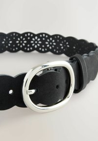 Ceinture en cuir noir avec un bord scallopé, des motifs floraux découpés au laser, une boucle en métal argenté et un ajustement réglable avec une boucle pour l'excès de longueur.
