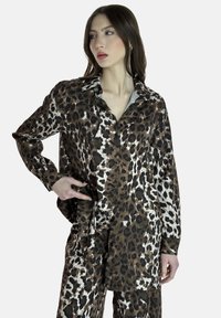Blusa in satin con stampa leopardata, maniche lunghe, colletto classico e chiusura a bottoni. Presenta tonalità di colore marrone, nero e bianco. Texture liscia.