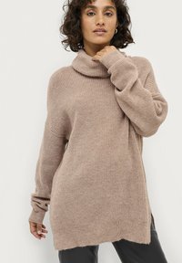 Beige, oversized sweater med en hættekrave, lavet af et blødt, struktureret strikmateriale. Har drop-skulder og ribbede manchetter.
